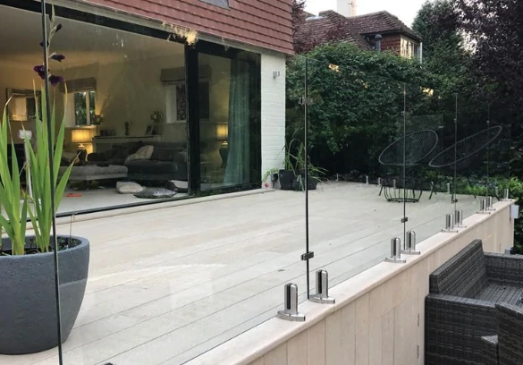 Elevated deck with semi-frameless glass railings and dark posts, contrasting with natural greenery and outdoor furniture.