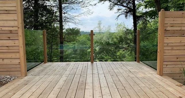 Rustic deck featuring glass panels with wooden frames, blending modern transparency with warm, natural charm in a forest setting.