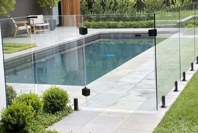 Modern swimming pool area with frameless glass fencing and a soft closing pool gate system, ensuring safety and sleek aesthetics. 